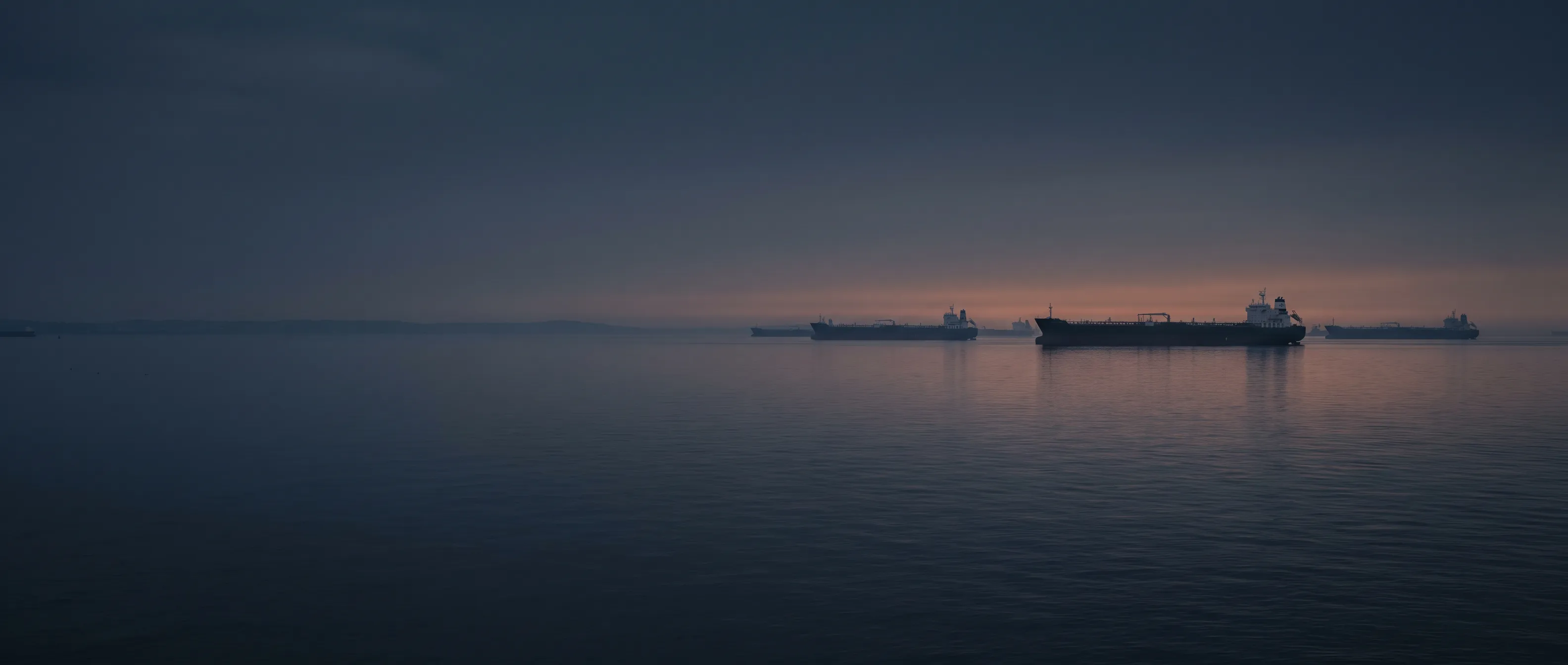 Tanker fleet silhouettes at anchor in evening light